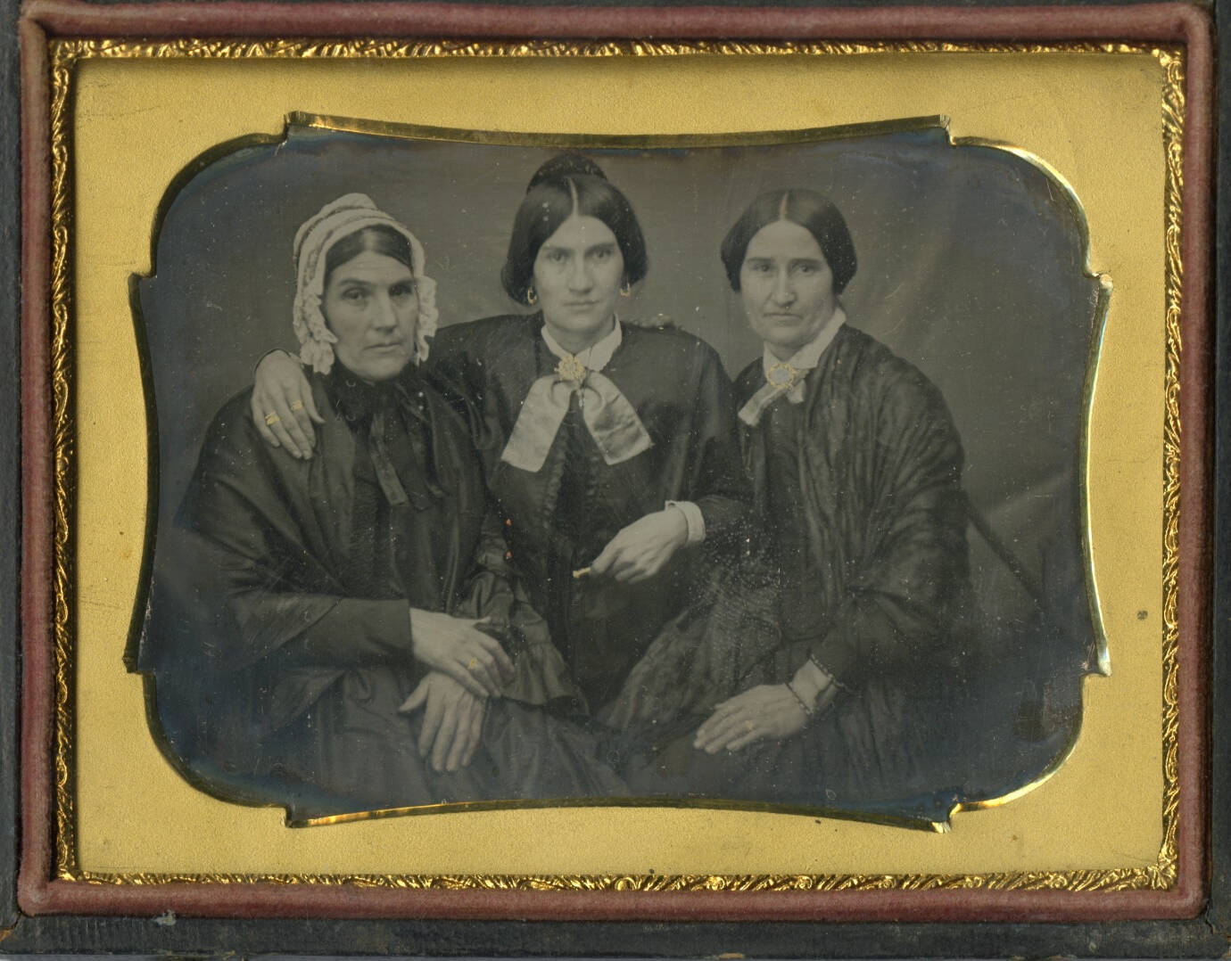 Historic photograph in a case with a gold frame, image is of three seated women all wearing dresses.